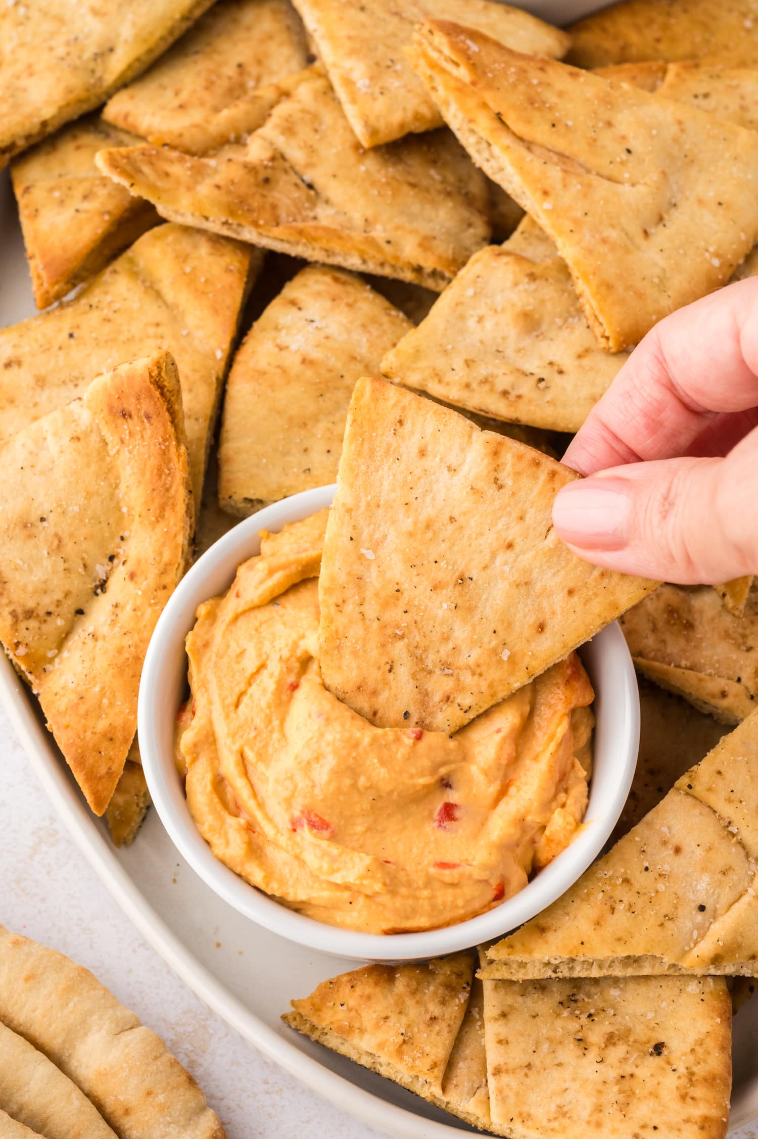 A close-up of a person dipping a pita chip into a bowl of hummus.