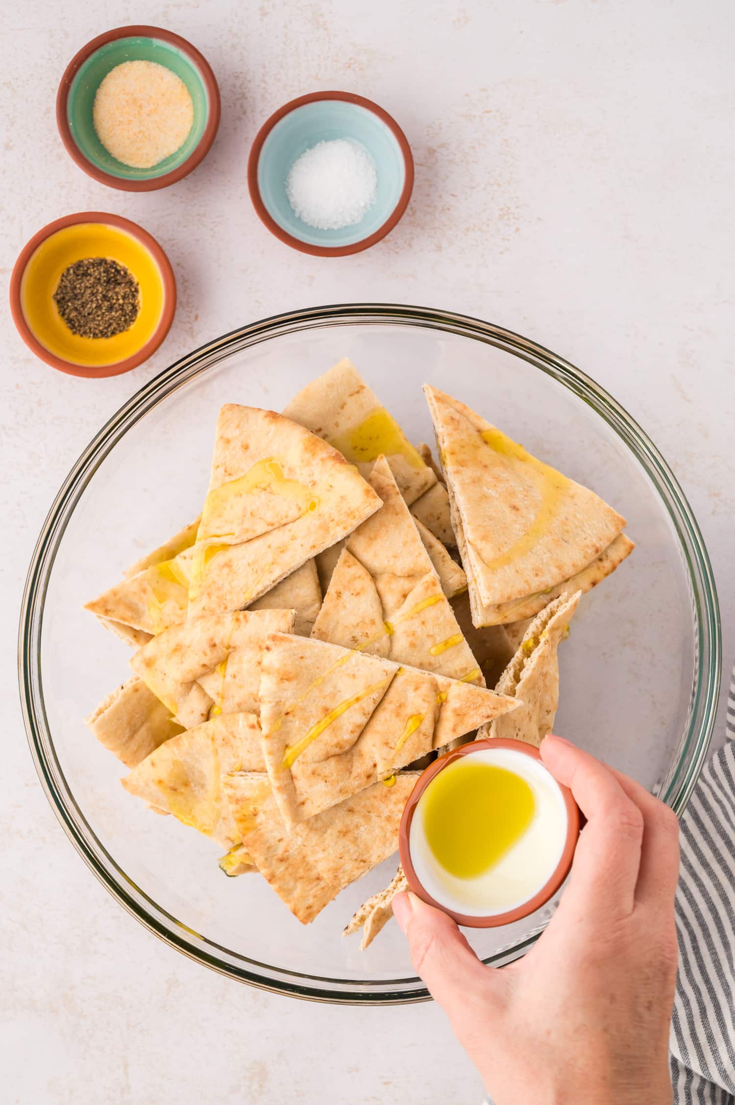 Pita triangles in a clear glass bowl with olive oil being drizzled on them.