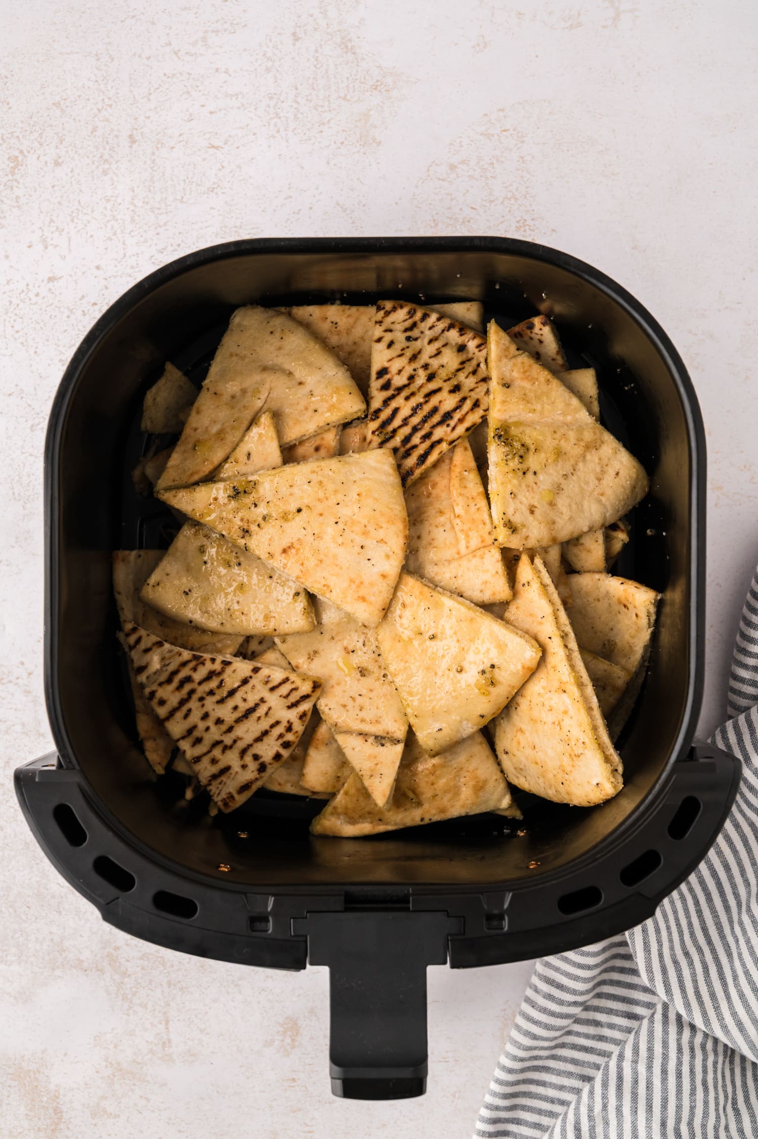 Pita wedges garnished with olive oil in an air fryer basket.