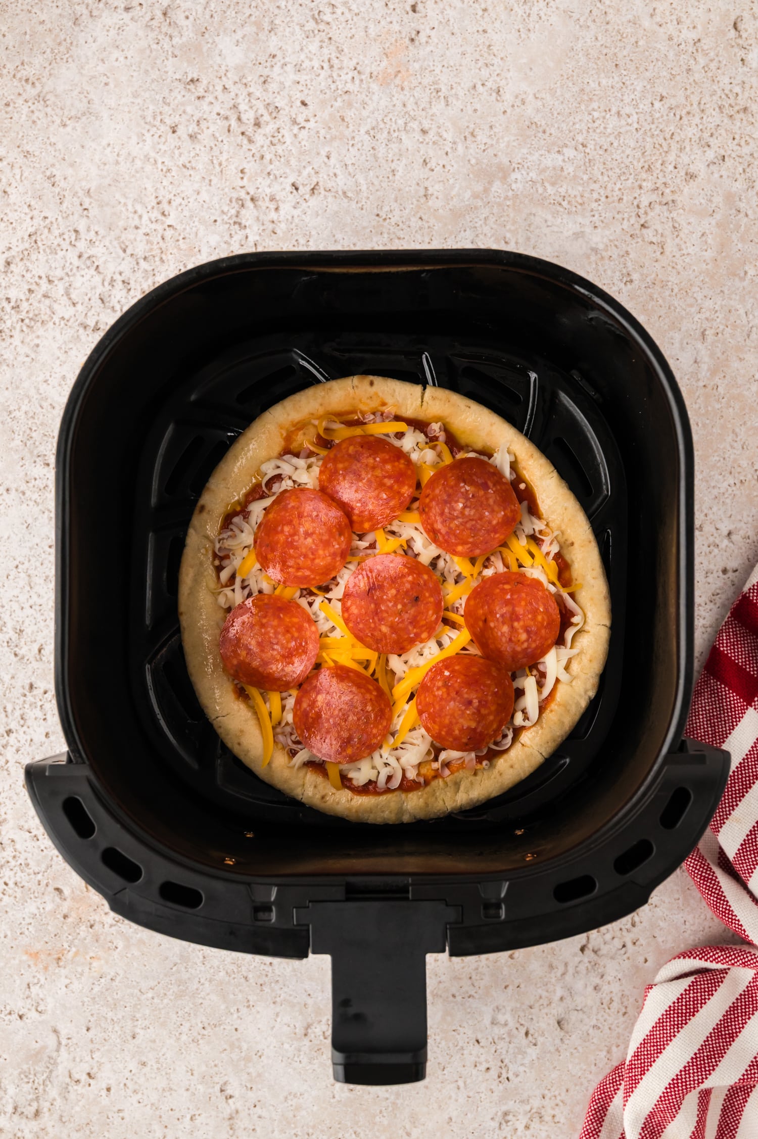 Overhead view of an uncooked pepperoni pita pizza in an air fryer basket.