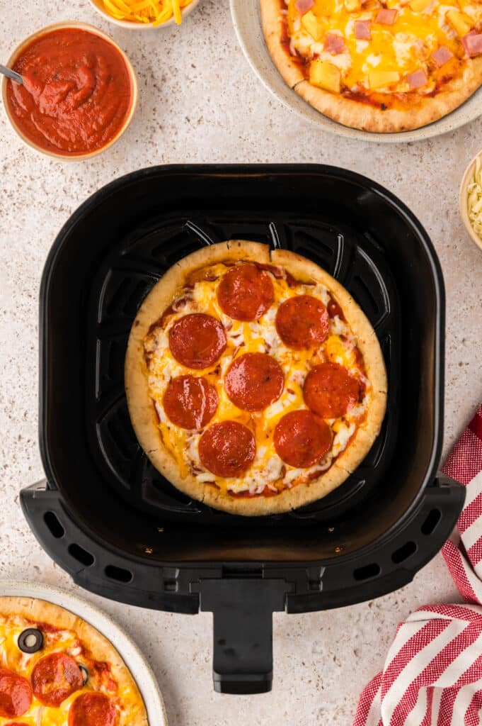 Overhead view of a cooked pepperoni pita pizza in an air fryer basket.