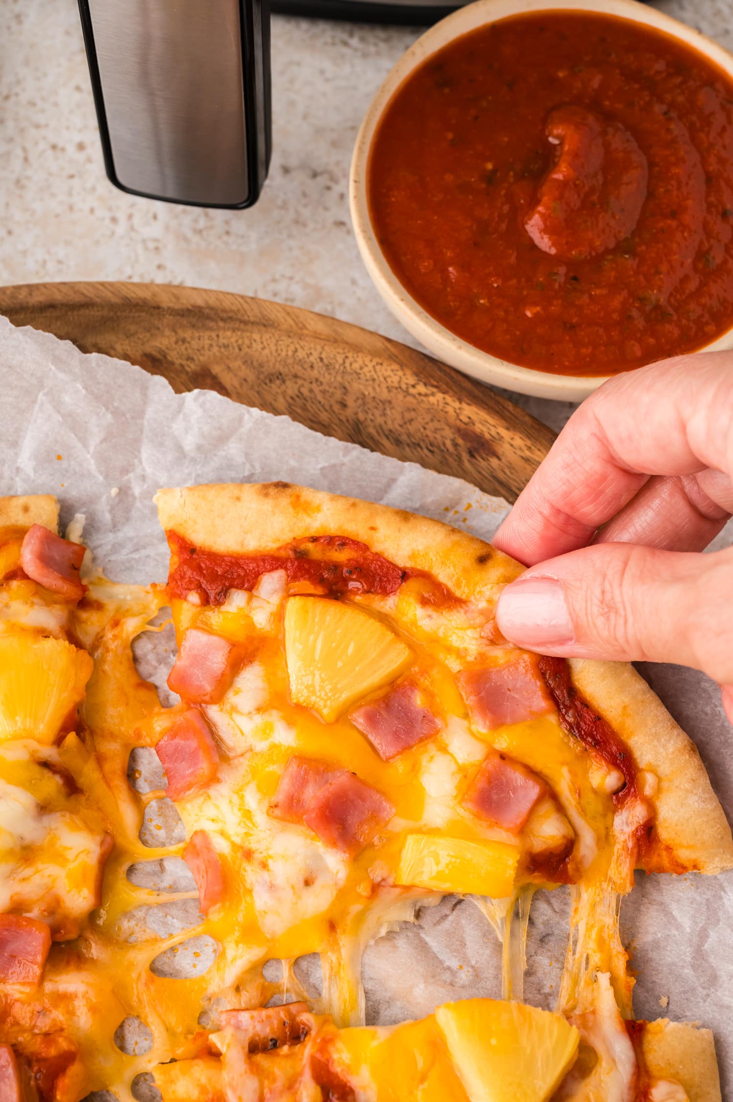 Close-up of a person's hand grabbing a slice of pita pizza.