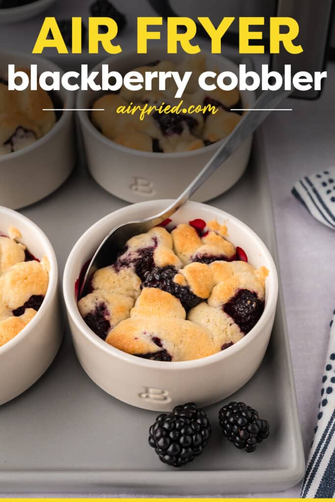 A spoon being dipped into a ramekin of blackberry cobbler resting on a tray.