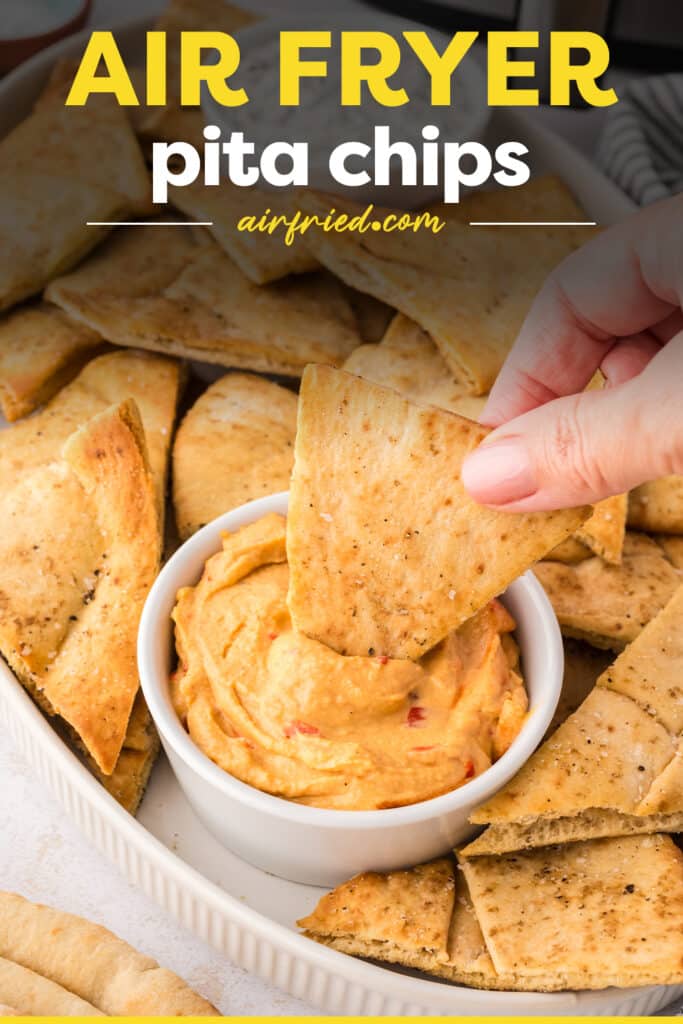 A pita chip is being dipped into a bowl of hummus.