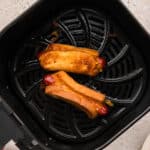 Overhead view of two grilled cheese hot dogs in an air fryer basket.