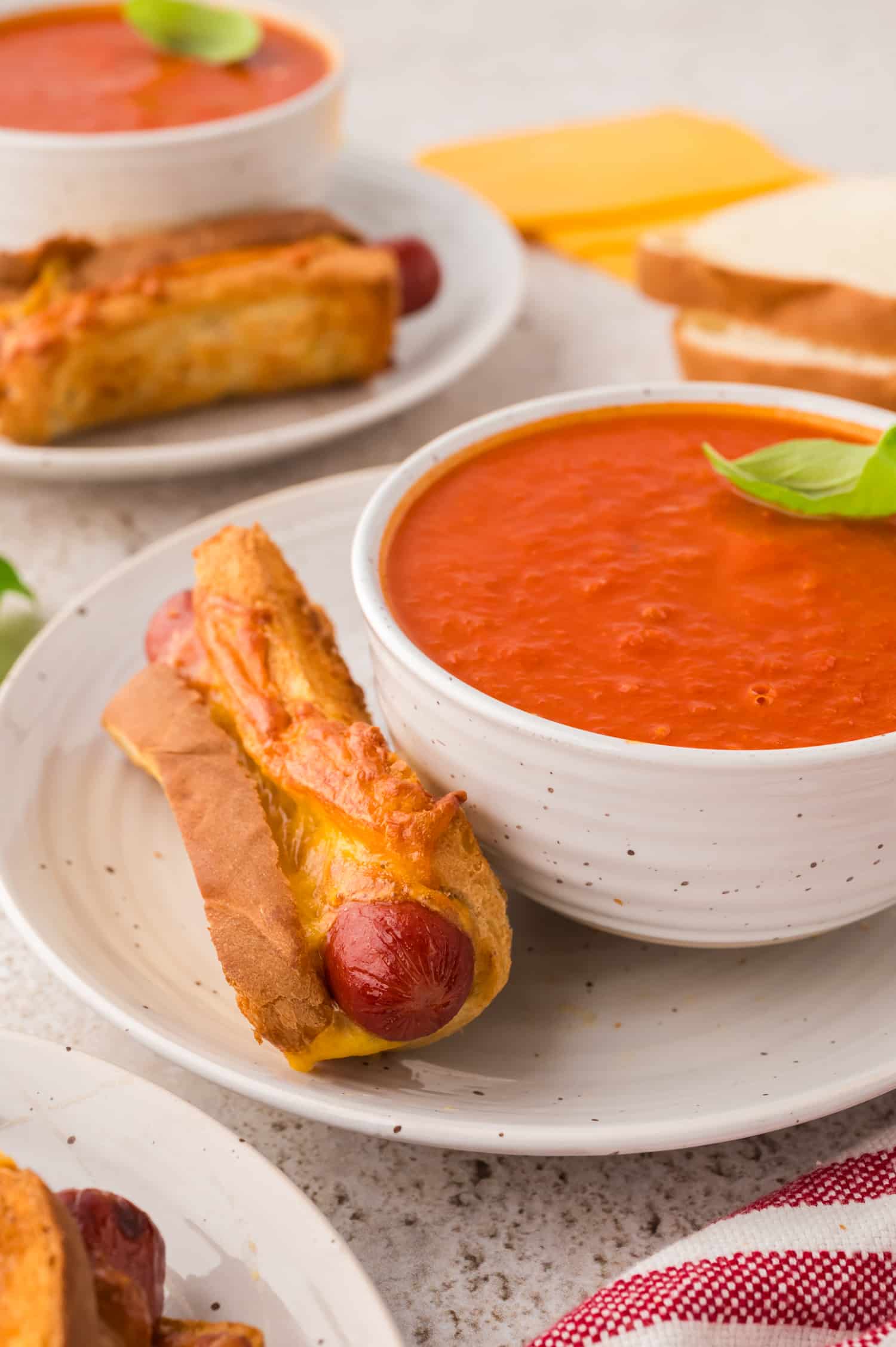 A grilled cheese hot dog and tomato soup on a white plate.
