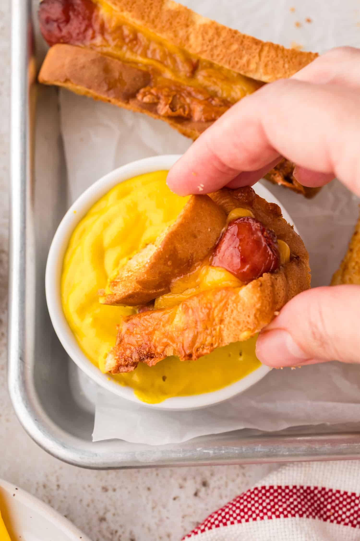 A grilled cheese hot dog being dipped into mustard.