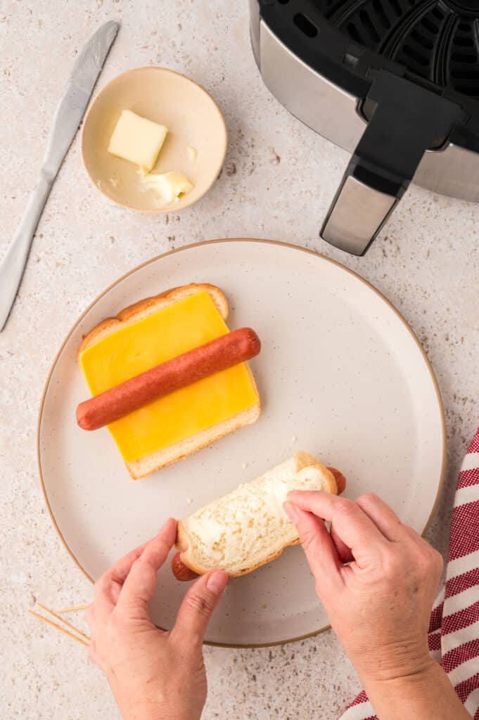 A person rolling a grilled cheese hot dog and putting toothpicks through it.