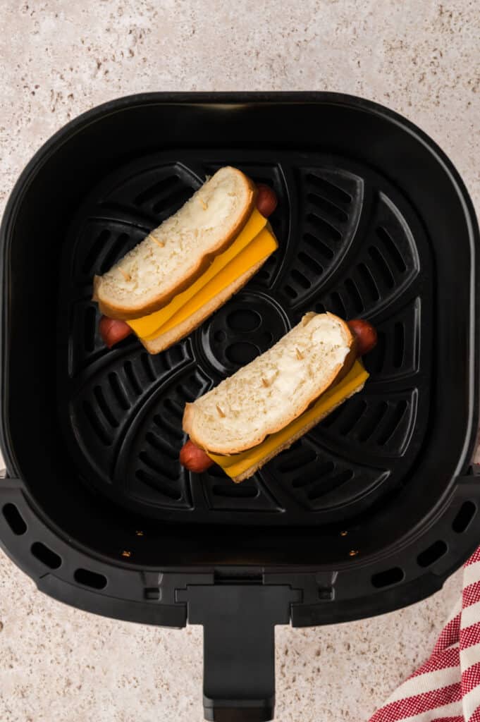 Two uncooked grilled cheese hot dogs in an air fryer basket.