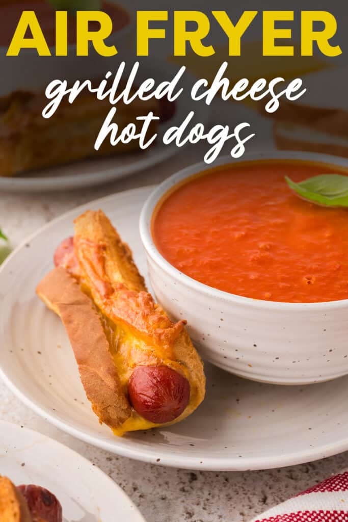 Close up of a plate with a grilled cheese hot dog next to a bowl of tomato soup.