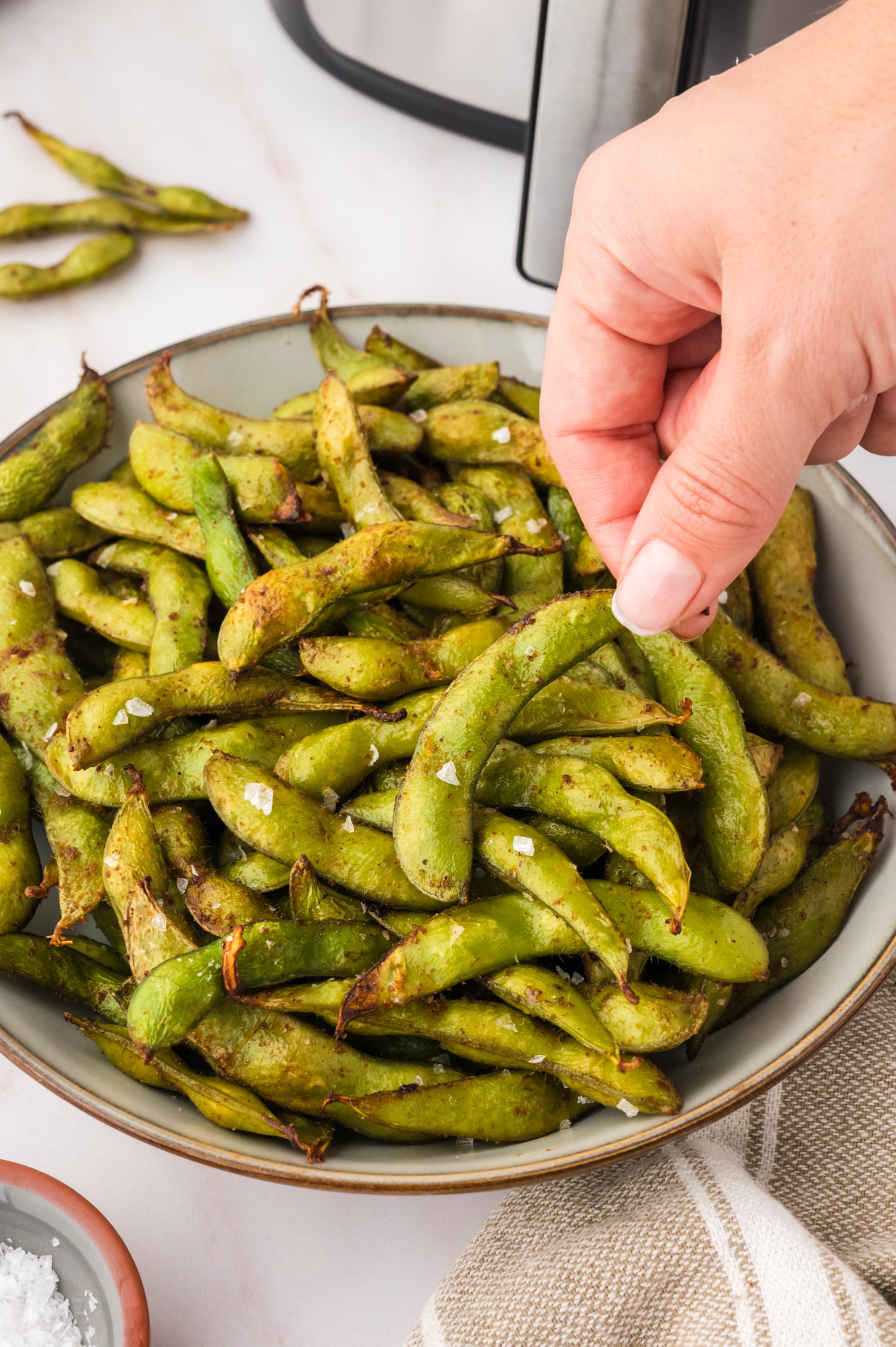 A person grabbing a cooked edamame off a plate.