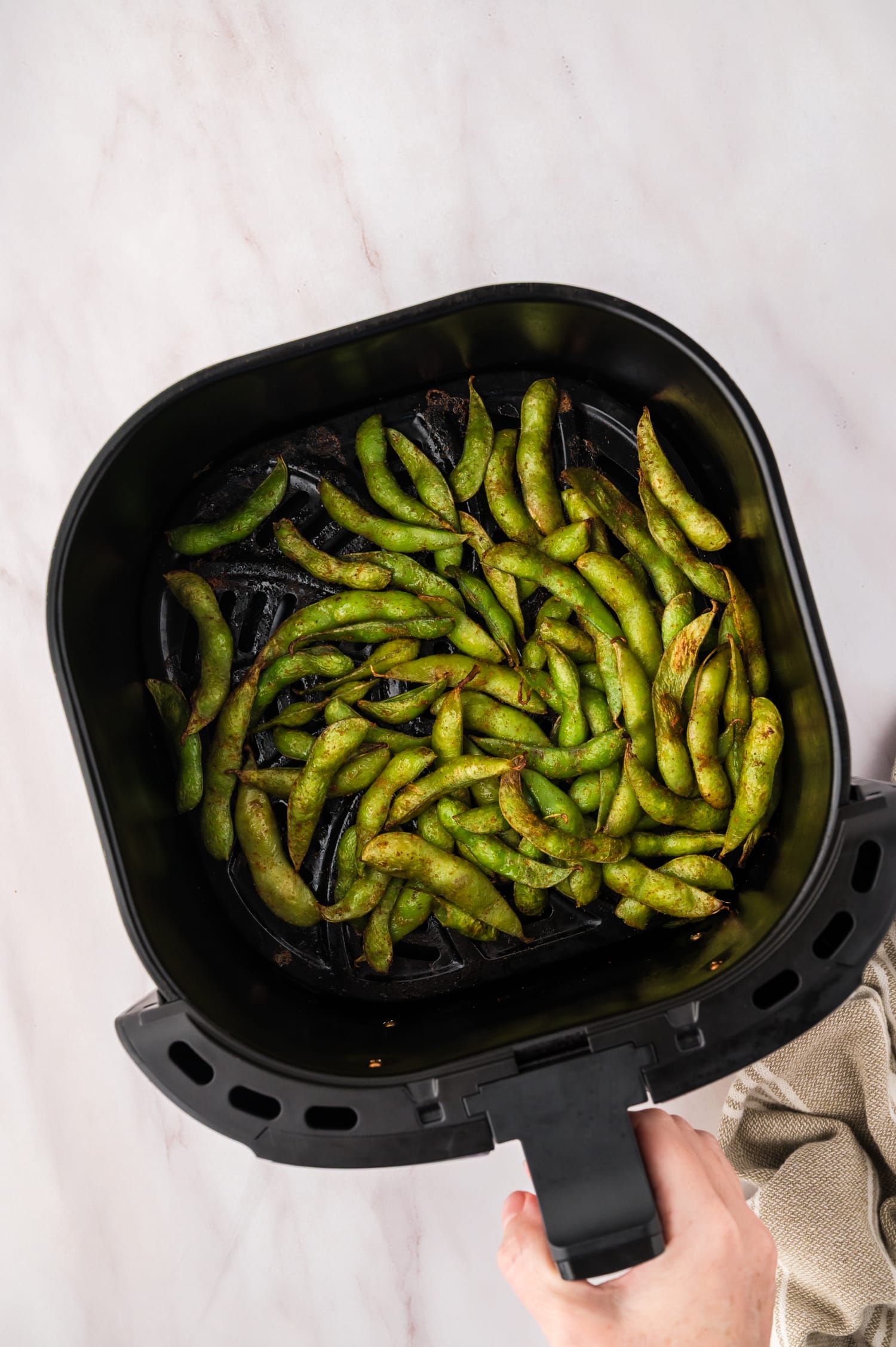Overhead view of edamame in an air fryer basket.