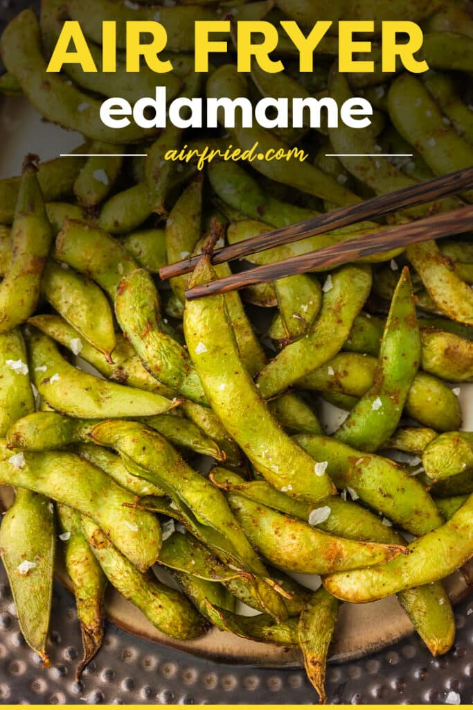 Close up of chopsticks grabbing an edamame off a plate.