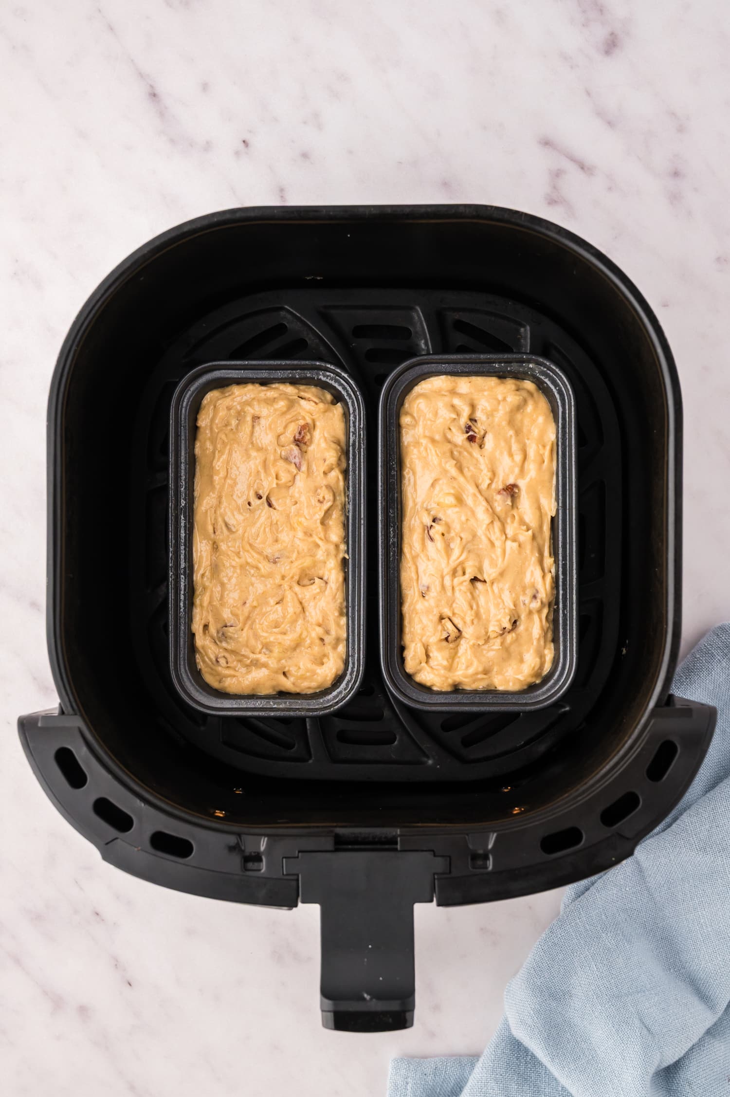2 small loaf pans with banana bread dough in an air fryer basket.