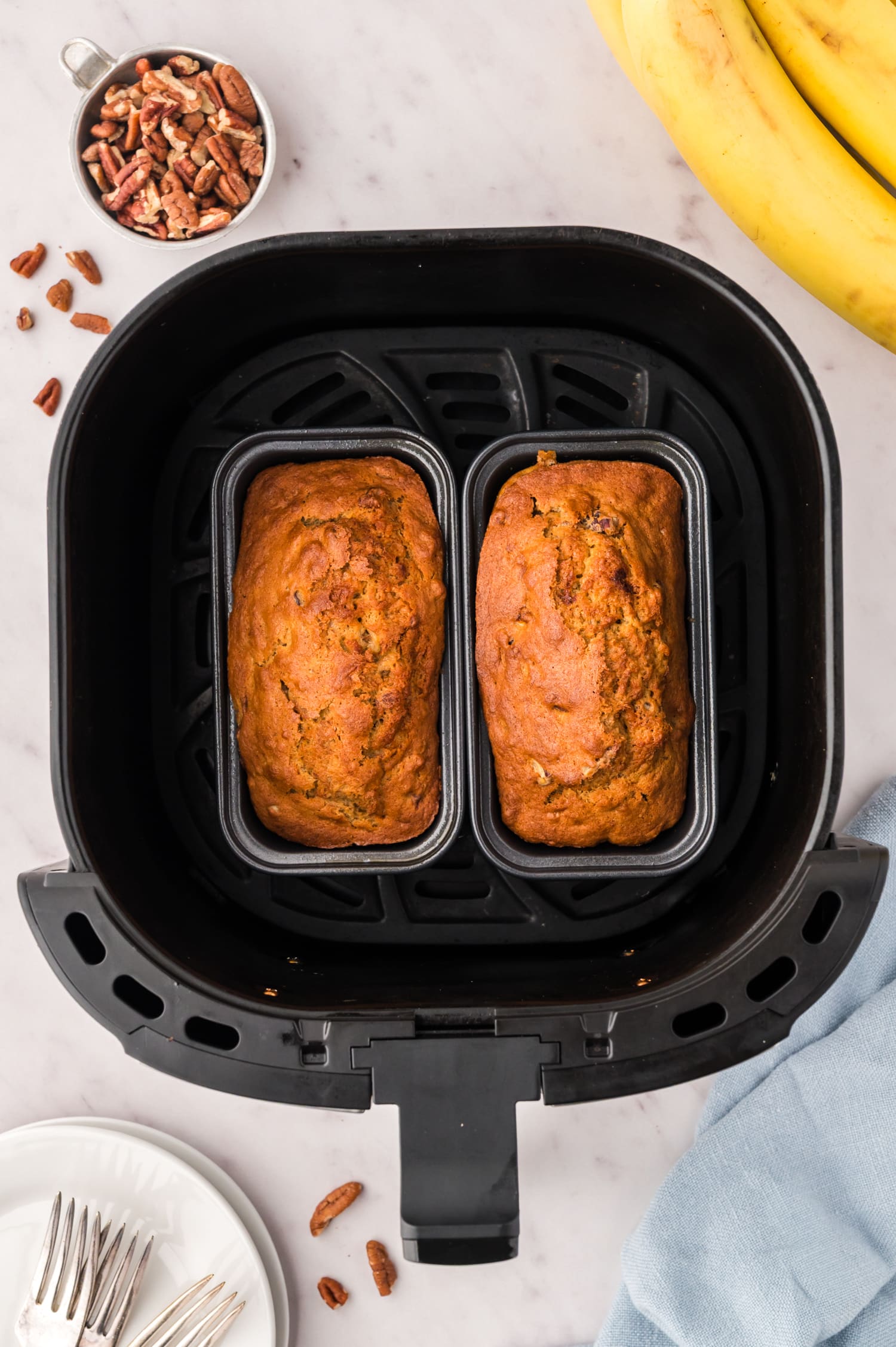 Two small loafs of banana bread in an air fryer basket.