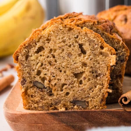 A slice of banana bread standing against a loaf of banana bread.
