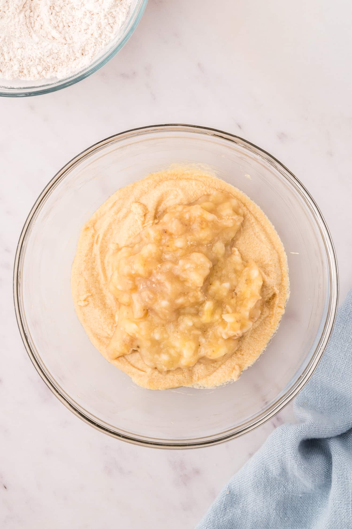 Ingredients for banana bread dough in a clear glass bowl.