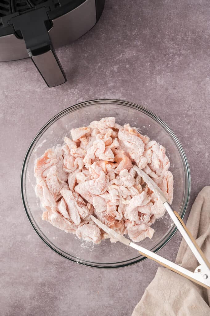 Raw chicken coated in breading in a clear glass bowl.