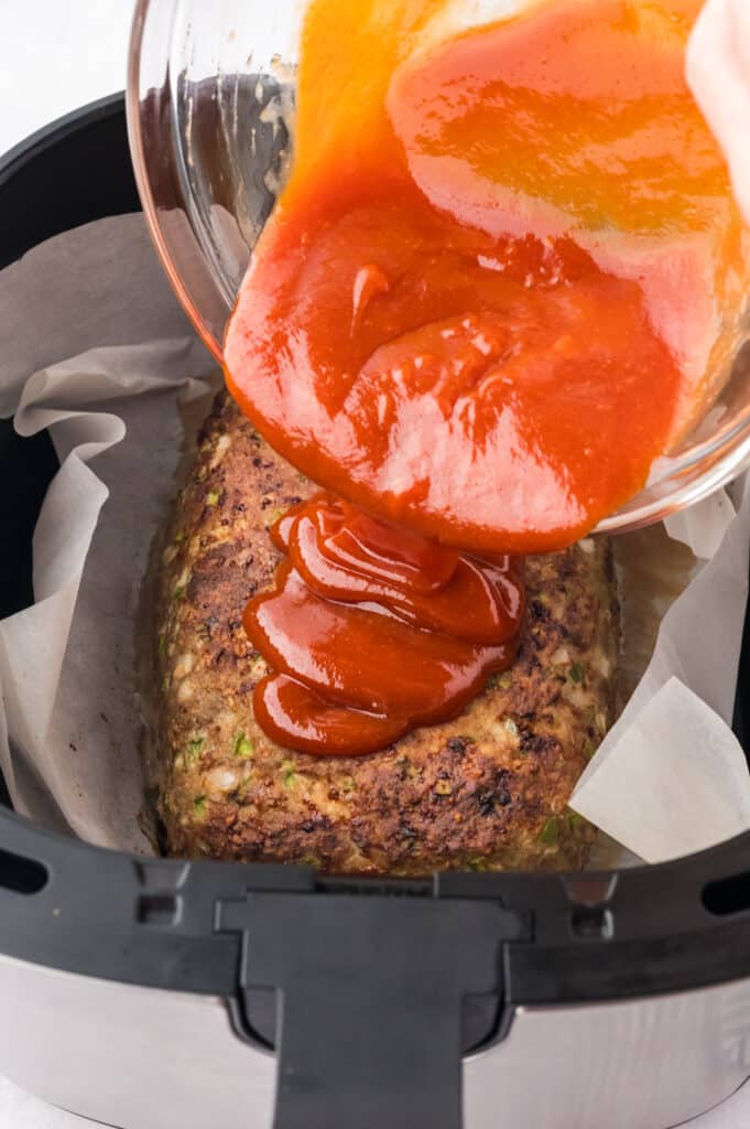 Glaze being poured onto a turkey meatloaf in an air fryer basket.