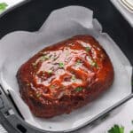 Meatloaf in an air fryer basket with a glaze on top.