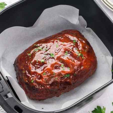 Meatloaf in an air fryer basket with a glaze on top.