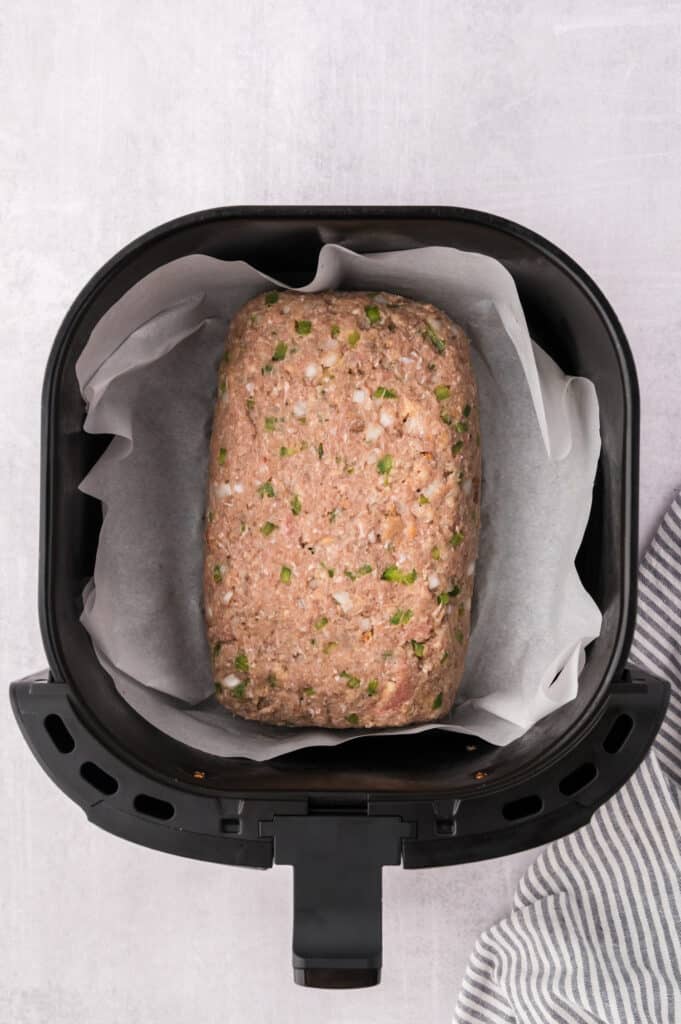Raw meatloaf on parchment paper in an air fryer basket.