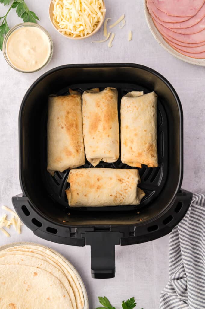 Four air fryer ham and cheese wraps inside an air fryer basket.