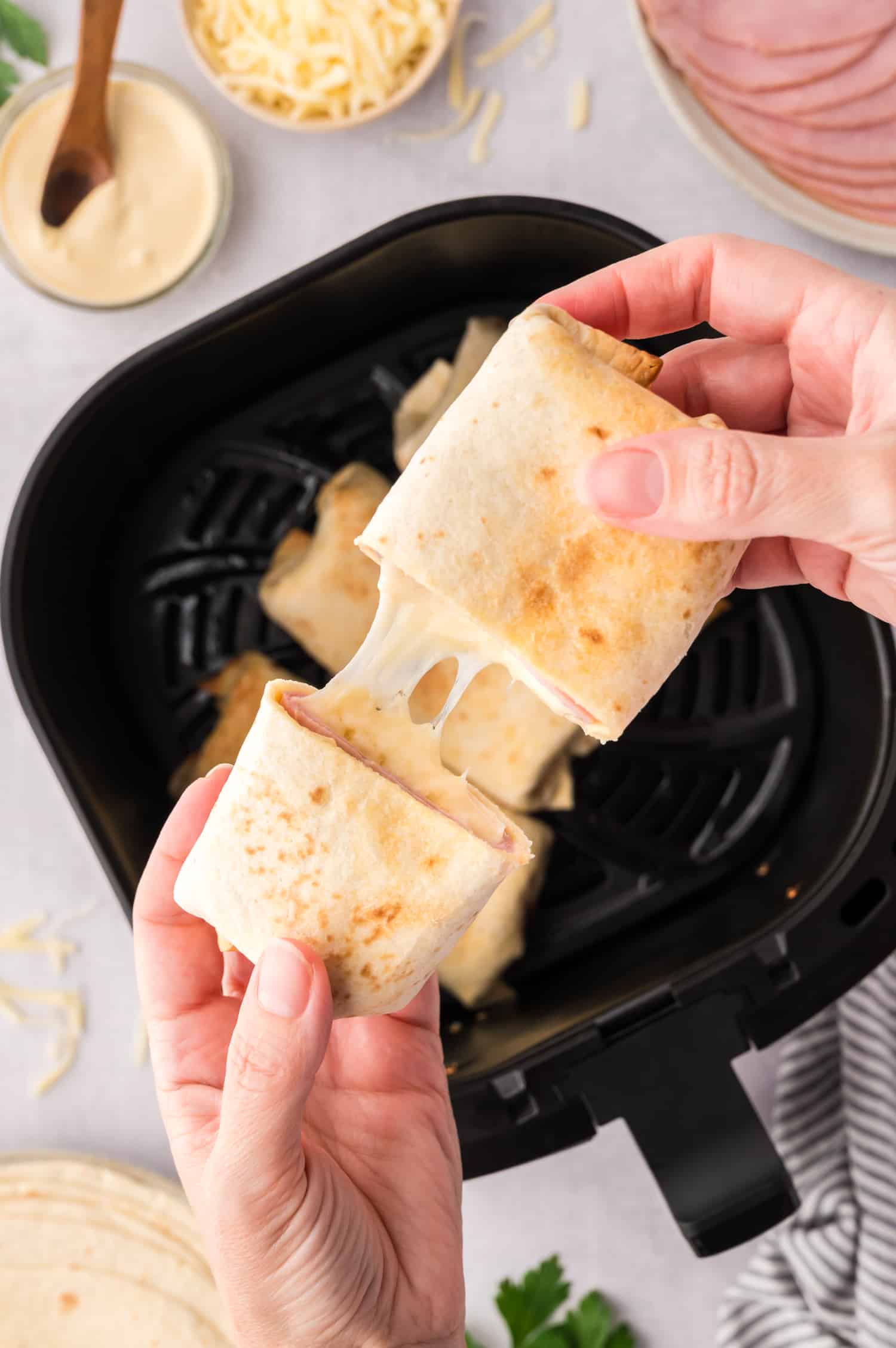 Overhead view of a person splitting an air fryer ham and cheese wrap, revealing the stringy melted cheese inside.
