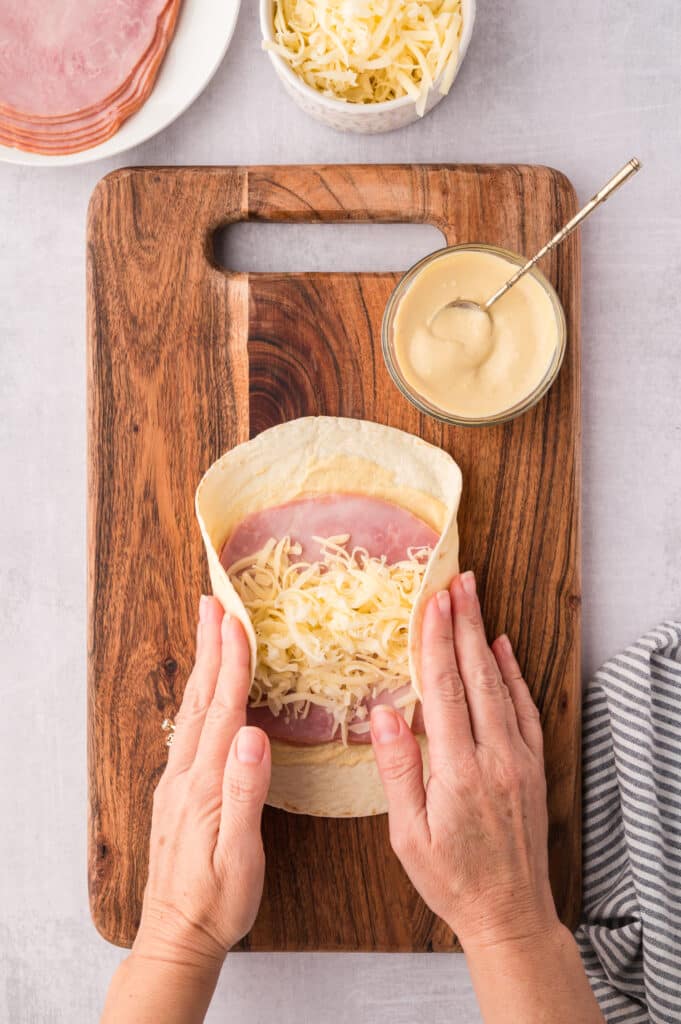 A woman's hands folding up an air fryer ham and cheese wrap.