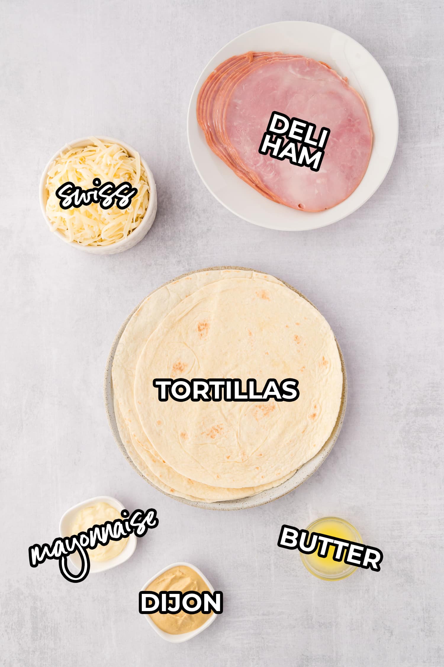Ingredients for air fryer ham and cheese wraps spread out on a white countertop, each labeled with a text overlay.